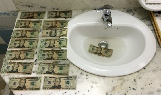 Wet twenty-dollar bills laid out to dry across a bathroom counter and in the sink